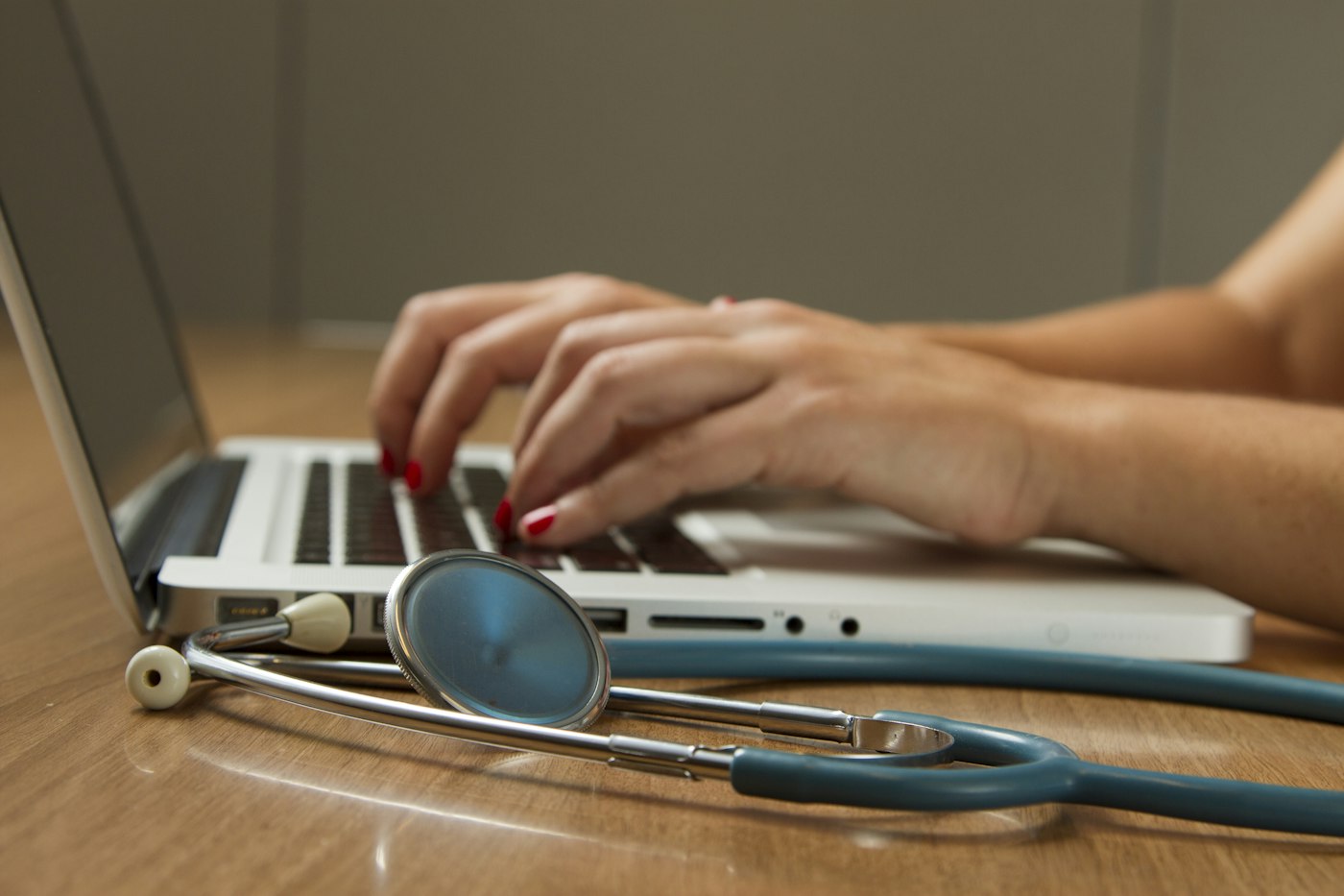 Hands writing beside a laptop and a stethoscope
