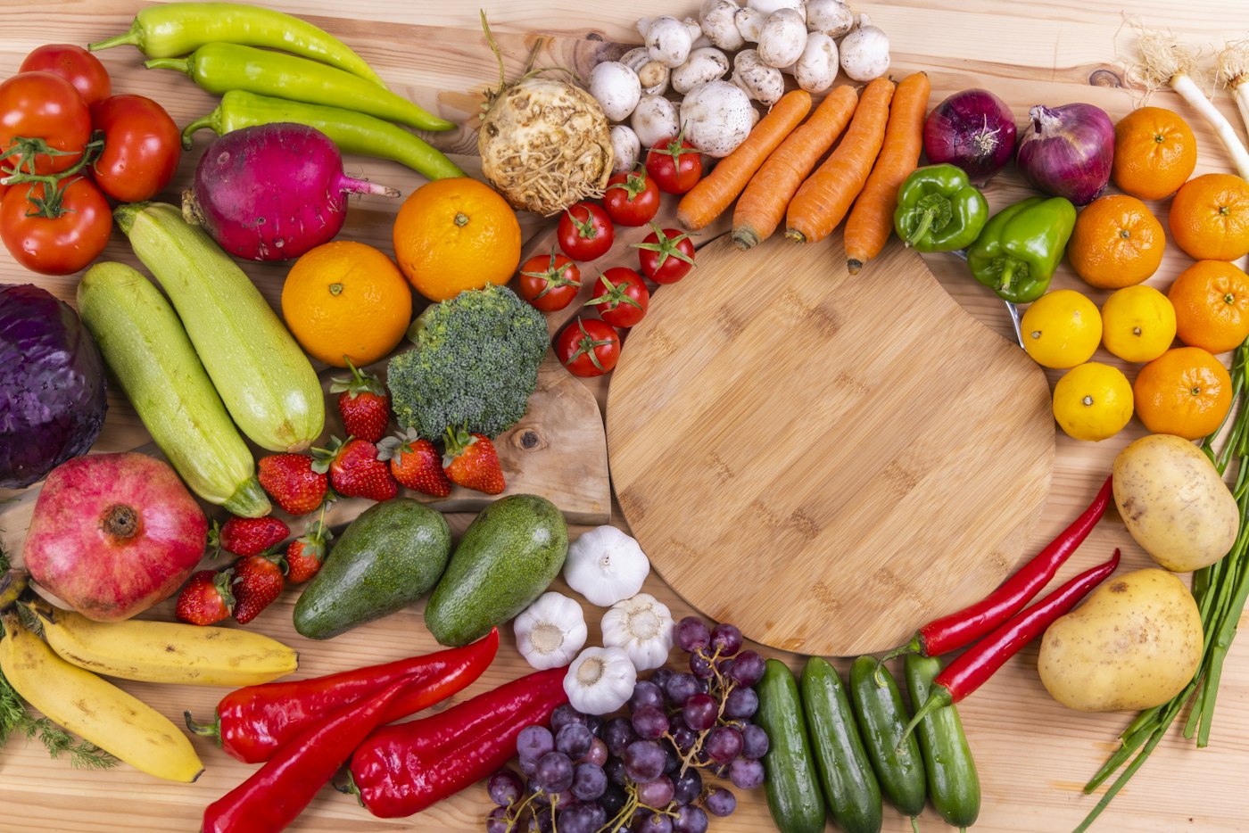 A wooden table covered with tomatoes, peppers, citrus, broccoli, and other fresh produce